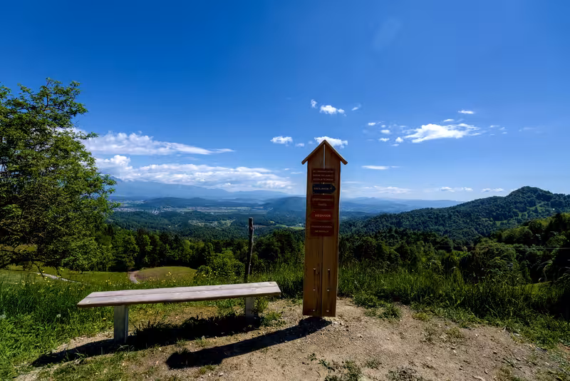 The bench, a signpost, and the view across the Ljubljana basin.